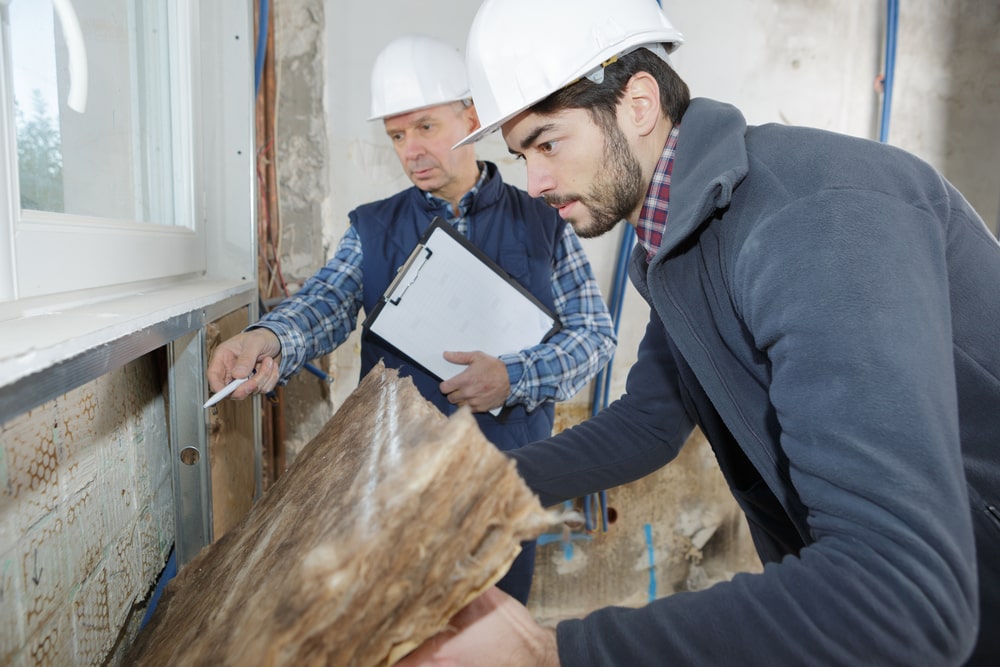 Two men wearing white hats looking into wall.